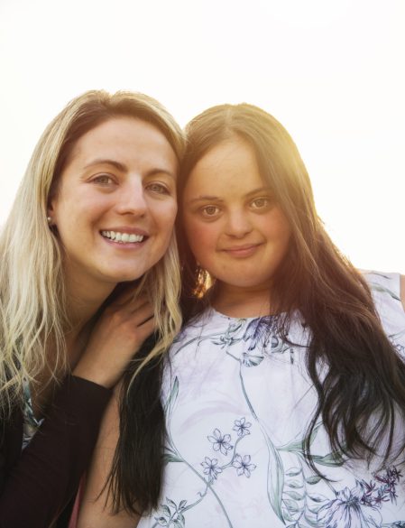 Portrait of trisomie 21 adult girl smilin outside at sunset with family friend